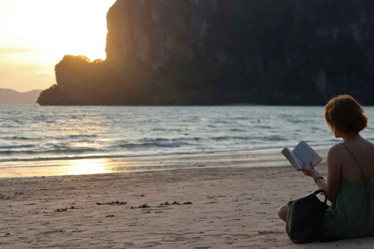 donna che legge in spiaggia in tramonto