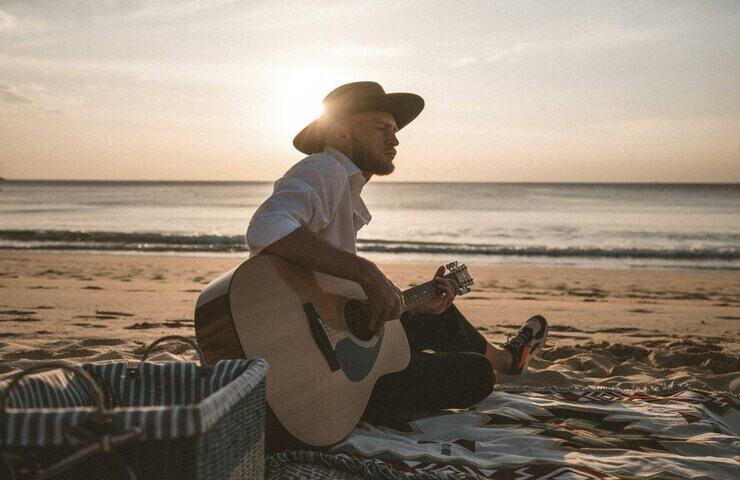 uomo suona chitarra in spiaggia al tramonto